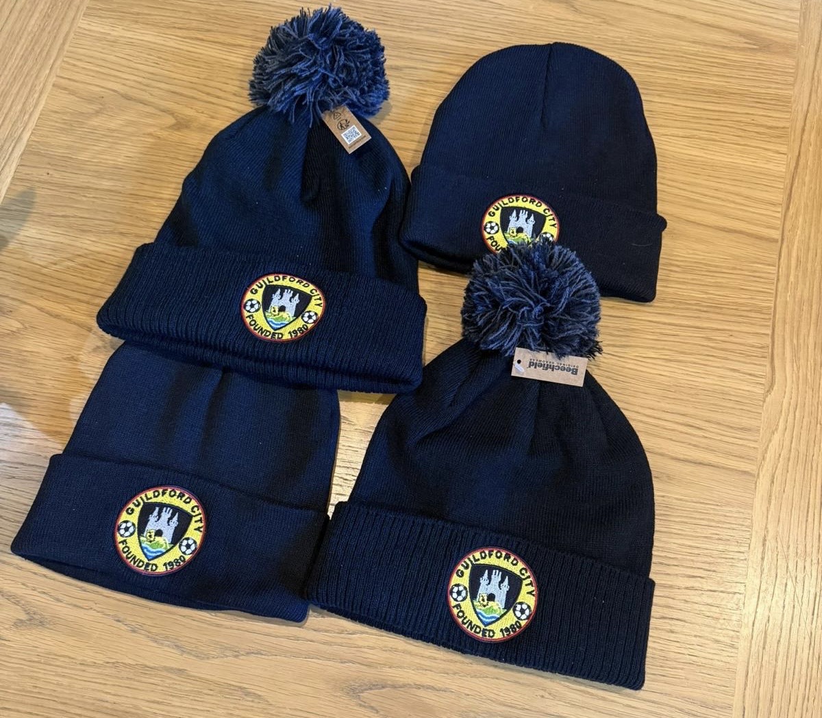 Four navy beanie and bobble hats with embroidered Guilford City badges